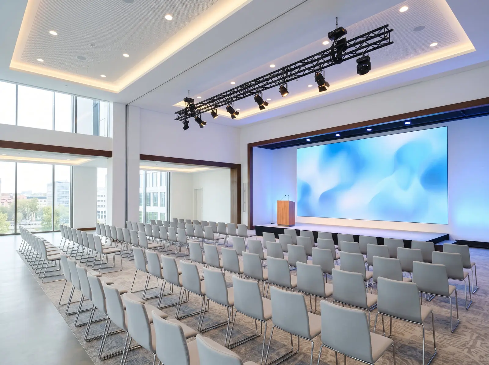 A conference hall set for an event, its LED wall above a low stage and rows of chairs under the house lights