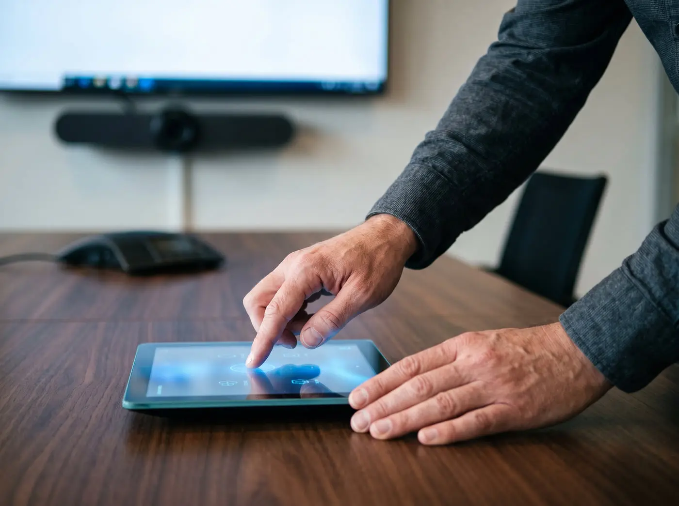 Hands adjusting a tabletop touch control panel in a meeting room